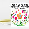 A folded greeting card with the text "MAY LOVE AND BRIGHTNESS SURROUND YOU TODAY" and a colorful floral illustration on the front.