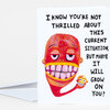 A folded greeting card with a white front printed with the text "I KNOW YOU'RE NOT THRILLED ABOUT THIS CURRENT SITUATION, BUT MAYBE IT WILL GROW ON YOU?" and a colorful cartoon face with a wide toothy grin, plus a tiny matching face near the bottom.