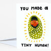 A folded greeting card with the text "YOU made a TINY HUMAN!" and a colorful illustration of a swaddled baby with radiating yellow marks.