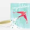 A folded greeting card with the word "congratulations" in white script above a red bird illustration on a teal background, with a white envelope partly visible behind it.