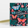 A folded greeting card with a black cover patterned with colorful butterflies and flowers and the white handwritten text "Happy Birthday".
