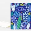 A folded greeting card with a blue cover featuring the words "Happy Birthday" in white script, a peacock illustration, and colorful leaf and flower motifs.