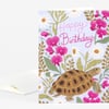A folded birthday card with a floral pattern, a turtle illustration, and the words "Happy Birthday" on the front.