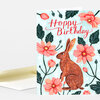A folded greeting card with a light blue floral design, a brown rabbit illustration, and the text "Hoppy Birthday" on the front.