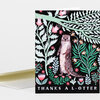 A folded greeting card with a black cover illustrated with an otter standing among pastel leaves and flowers, and the text "THANKS A L-OTTER" at the bottom.