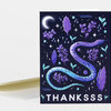 A folded greeting card with a dark purple cover featuring a stylized snake, leaves, stars, and a crescent moon, with the word “THANKSSS” printed in large white letters at the bottom.