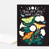 A greeting card with a black front featuring the handwritten phrase “you are my moon & stars,” crescent moons and stars, and colorful moths and flowers.