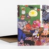 A folded greeting card with an illustrated Halloween scene of children carving pumpkins, hanging ghost and bat decorations, and a black cat in a room.