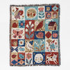 A woven blanket with fringe edges featuring a patchwork grid of whimsical illustrations including a sun face, flowers, birds, a butterfly, a mushroom, a house, a snail, a cat, and geometric motifs in red, blue, tan, and cream.