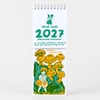 A spiral-bound wall calendar with a white cover printed in green and orange, showing the text "Phoebe Wahl 2027 Postcard Calendar" and an illustration of a small figure holding a mushroom on the front above a mushroom scene below.