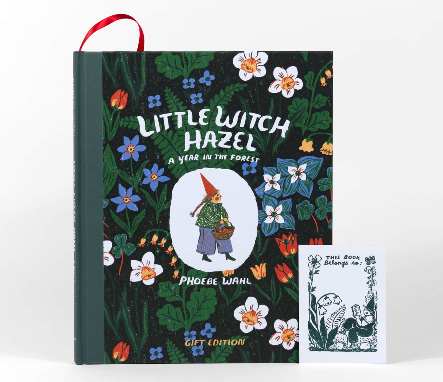 A hardcover book titled "Little Witch Hazel: A Year in the Forest" by Phoebe Wahl, with a floral cover illustration and a separate bookmark or bookplate insert that reads "This Book Belongs to:".