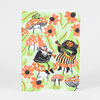 A small notebook with a rounded-corner cover illustrated with gnomes playing music among orange flowers and mushrooms in green, orange, black, and white.