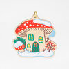 A mushroom-shaped house ornament with a red spotted cap, a green door, small windows, and a gold hanging loop.