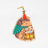 A hedgehog-shaped ornament with a gold hanging loop, wearing a red party hat and green cape and playing a small drum.