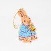 A rabbit-shaped ornament with a hanging gold cord, illustrated holding a yellow horn and wearing a blue patterned coat.