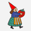A colorful enamel pin shaped like a gnome woman with a tall red hat, blue top, teal skirt, and striped apron holding a large strawberry.