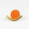 A snail-shaped enamel pin with a gold outline, bright orange spiral shell, and beige body with small red dots.