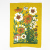 A yellow tea towel printed with a tall garden scene of white and orange flowers, green leaves, butterflies, a frog, and mushrooms.