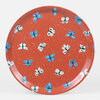 A small round tray with a terracotta-orange surface patterned with scattered blue, white, and green butterfly illustrations.
