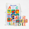 A set of wooden ABC blocks with colorful hand-painted letters and illustrated animal, fruit, mushroom, rainbow, house, clover, piano, moon, sun, and other picture faces, shown with a drawstring storage bag printed with matching ABC block artwork and the name "Phoebe Wahl".