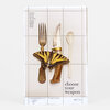 A printed art poster showing a fork, knife, and spoon arranged with a yellow-and-black butterfly and the text "choose your weapon," plus a vertical list of words at upper left and a handwritten edition number at the bottom right.