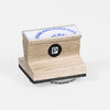 A small wooden rubber stamp with a white top label reading "MORE MAIL MORE MAIL" in blue arched text, a black circular logo with a white "P" on the side, and a black foam base.