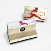 A rubber stamp with a red devil figure running across a rectangular banner and a small curved arrow detail, mounted on a wooden block with a clear top and a black circular logo with a white "P".