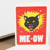 A greeting card with a red front featuring a black cat head in a yellow burst and the large white text "ME-OW".