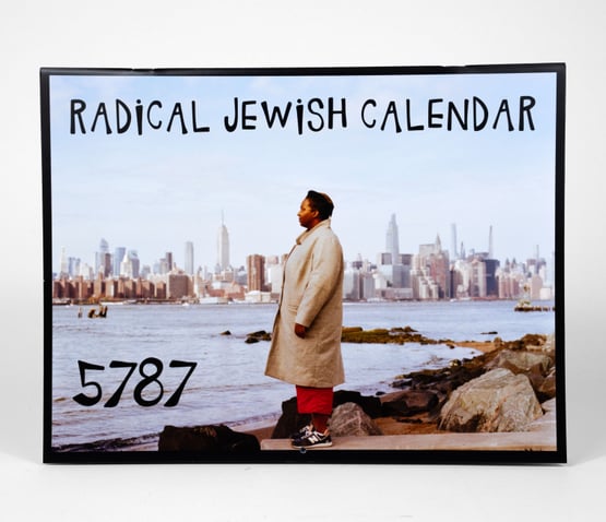 A calendar cover showing the text "RADICAL JEWISH CALENDAR" and "5787" above a person standing by the water with a city skyline in the background.