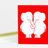 A red greeting card featuring two white elephants facing each other with intertwined trunks.