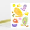 A folded greeting card with a white front printed with colorful abstract butterfly and flower shapes in yellow, green, purple, orange, and pink.