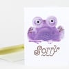 A folded greeting card with a purple toad illustration and the word "Sorry" in stylized brown lettering on the front.