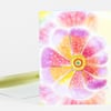 A folded greeting card with a large colorful open flower illustration in pink, purple, yellow, and orange on the front.