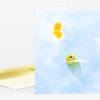 A folded greeting card with a pale blue cover featuring a small yellow butterfly near the top and a green tadpole illustration near the lower right, with a matching yellow envelope partly visible behind it.
