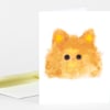 A folded white greeting card with a fuzzy orange cat illustration on the front, featuring round black eyes, a small pink nose, and white whiskers.