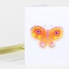 A folded white greeting card with a colorful butterfly face illustration in orange, pink, yellow, and purple on the front.