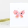 A white greeting card featuring a pink butterfly with a smiling face, curly antennae, and colorful wing details, shown with a matching envelope.