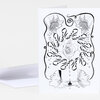 A folded greeting card featuring a black-and-white abstract illustration with mirrored hands holding pomegranate seeds at the top, a central rose-like flower, two profile faces at the bottom, and small initials near the lower edge.
