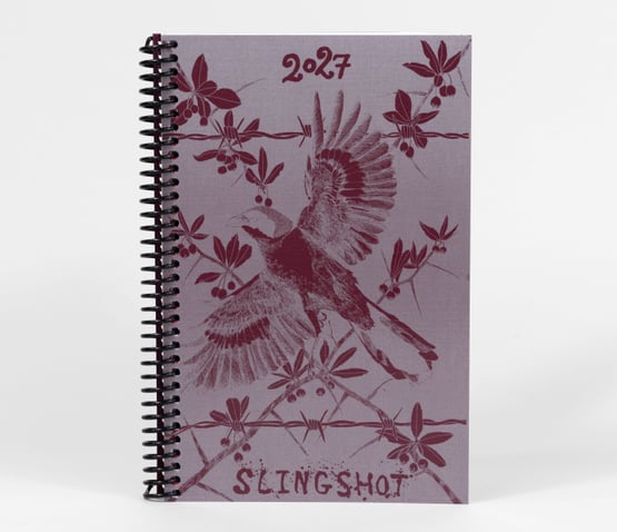 A planner cover with an orange-and-black illustrated design showing butterflies, a wheel-like calendar graphic, the year "2027," and the word "SLINGSHOT" near the bottom, with a large "Cover TBA" overlay across the center.