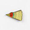 A small bird-shaped enamel pin with a red head, yellow beak, turquoise neck stripe, cream patterned body, and black eye.