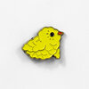 A small yellow chick-shaped enamel pin with a black eye, orange beak, and dotted feather details outlined in metal.