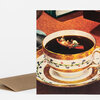 A folded greeting card with a brown envelope, featuring an illustration of a coffee cup filled with dark coffee and a tiny canoe with two people floating in the cup.