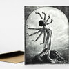 A black-and-white greeting card shows a figure with multiple outstretched arms standing on a rocky surface in front of a large circular moon-like shape.