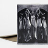 A black-and-white greeting card shows five women in long dresses with raised arms beneath a crescent moon, with a matching envelope partially visible behind it.