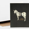 A black greeting card with a stylized zebra illustration and the words "Happy Birthday" in tan lettering.