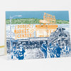 A folded greeting card featuring a blue, orange, and white illustration of Pike Place Market with visible signs reading "PUBLIC MARKET CENTER," "FARMERS MARKET," "Pike Pl," "POST ALLEY," and "YIELD TO PEDESTRIANS."