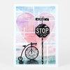 A postcard featuring a collage-style illustration of a black stop sign reading "STOP IN THE NAME OF LOVE," a street sign reading "NW LOVEJOY ST," and a decorative tricycle in front of a large pink heart.