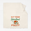 An off-white cloth towel printed with the text "EAT MORE Streamlined FRUIT" and a stylized orange, green, and white fruit illustration.