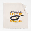 A cream-colored cloth with a printed graphic of a frying pan holding two eggs and the text "It Tastes Better HOME MADE".