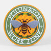 A round green and orange sign with a large bee over a flower and the words “POLLINATOR WORK ZONE” around the edge.